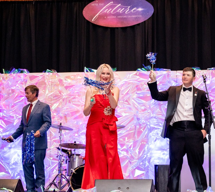 Three people on stage twirling metallic streamers.